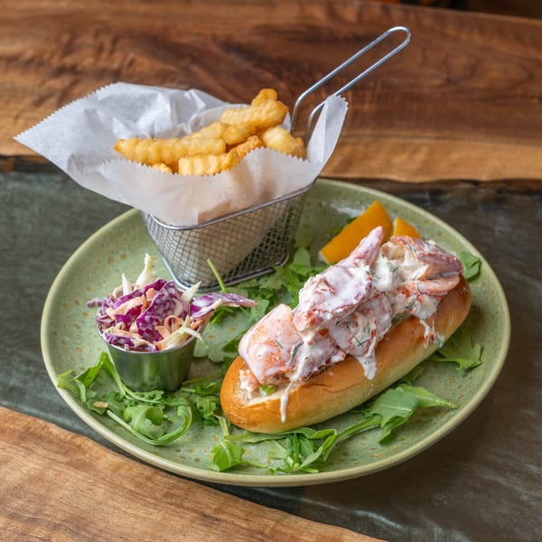 Lobster roll with fries and coleslaw on a green plate, garnished with arugula.