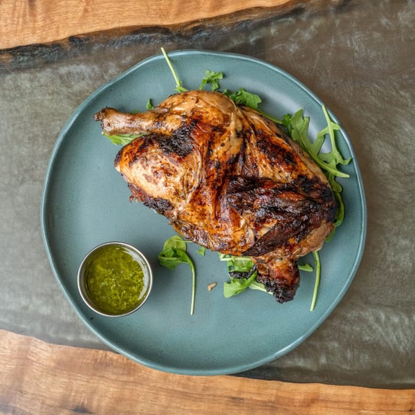 Grilled chicken with crispy skin, served on a bed of arugula with a side of green sauce.