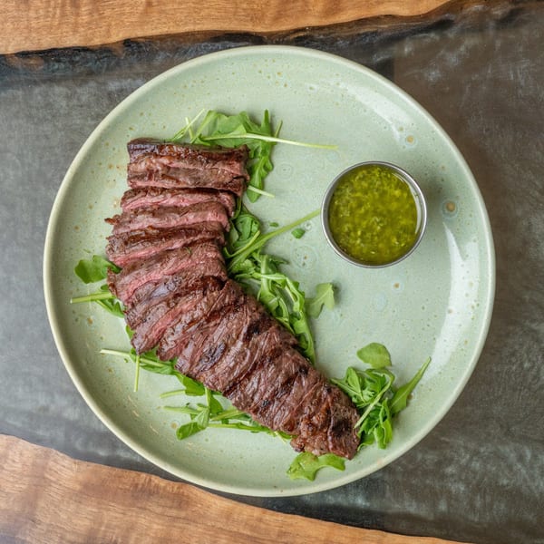 Grilled skirt steak, sliced and fanned over arugula, with a side of green chimichurri sauce.