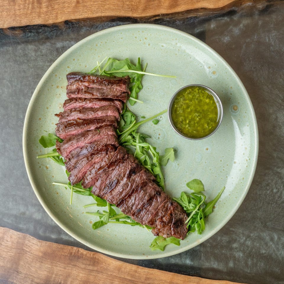 Grilled skirt steak, sliced and fanned over arugula, with a side of green chimichurri sauce.