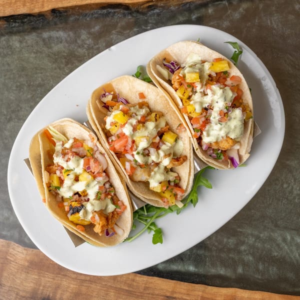 Three fish tacos with pineapple salsa and creamy sauce on a white plate with arugula.