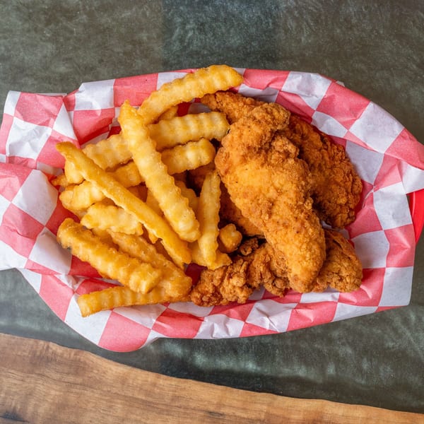 Crispy chicken tenders and crinkle-cut fries in a red and white checkered paper-lined basket.