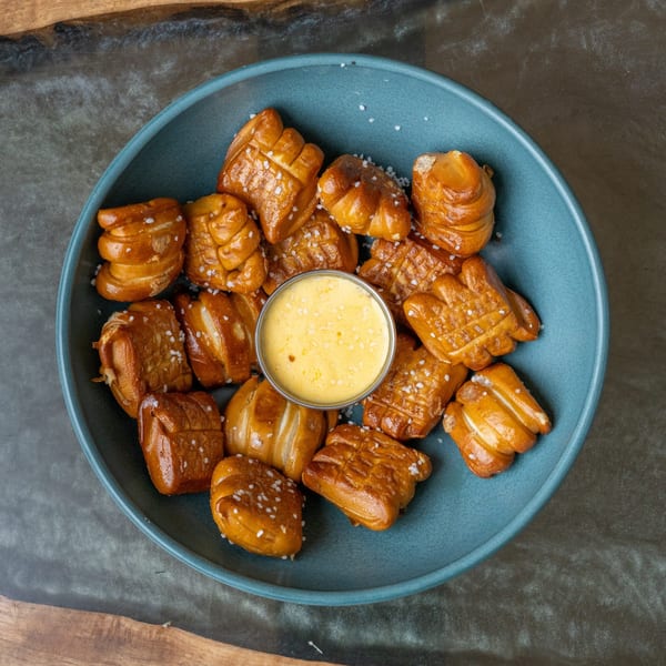 Salted pretzel bites with a side of cheese dip in a blue bowl.