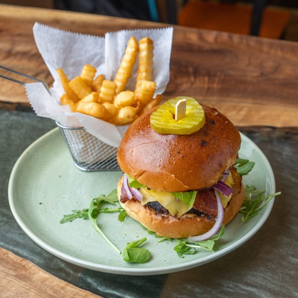 A gourmet burger with cheese, bacon, red onion, and arugula, served with crinkle-cut fries.
