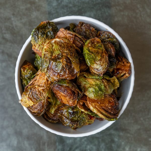 Crispy roasted Brussels sprouts, golden brown and green, served in a white bowl on a dark background.