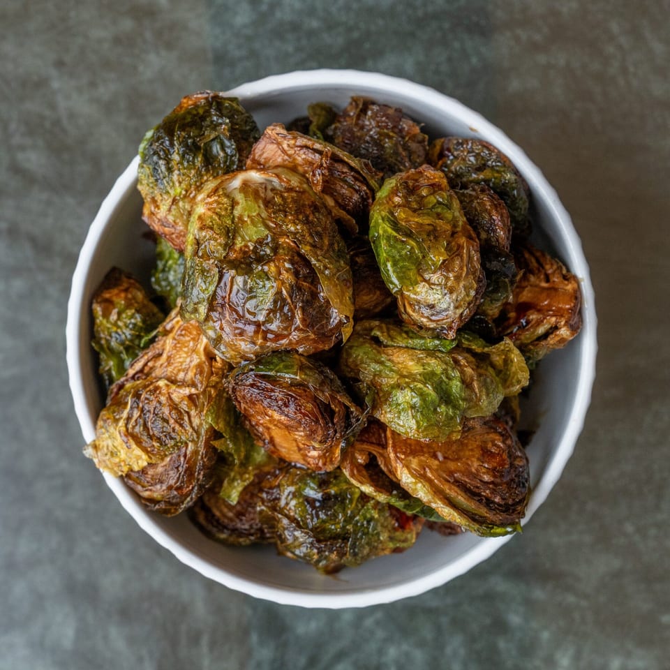 Crispy roasted Brussels sprouts, golden brown and green, served in a white bowl on a dark background.