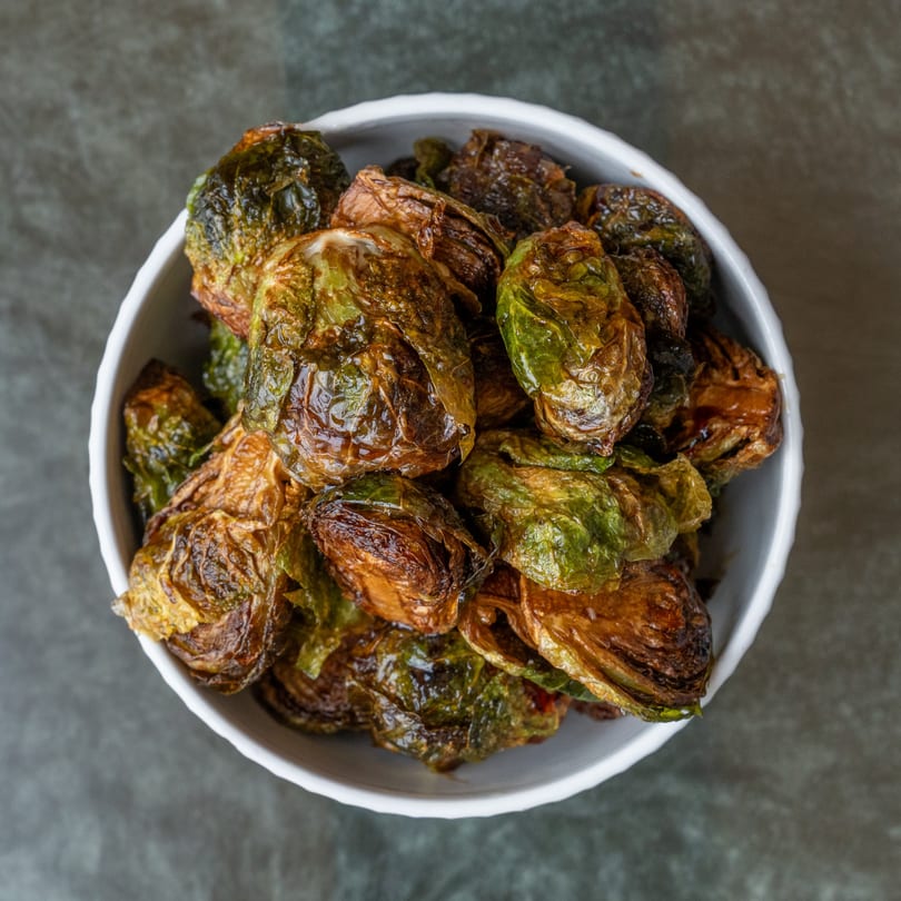 Crispy roasted Brussels sprouts, golden brown and green, served in a white bowl on a dark background.