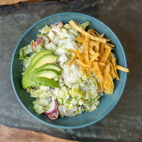 Overhead view of a salad with avocado, cheese, and tortilla strips in a blue bowl.